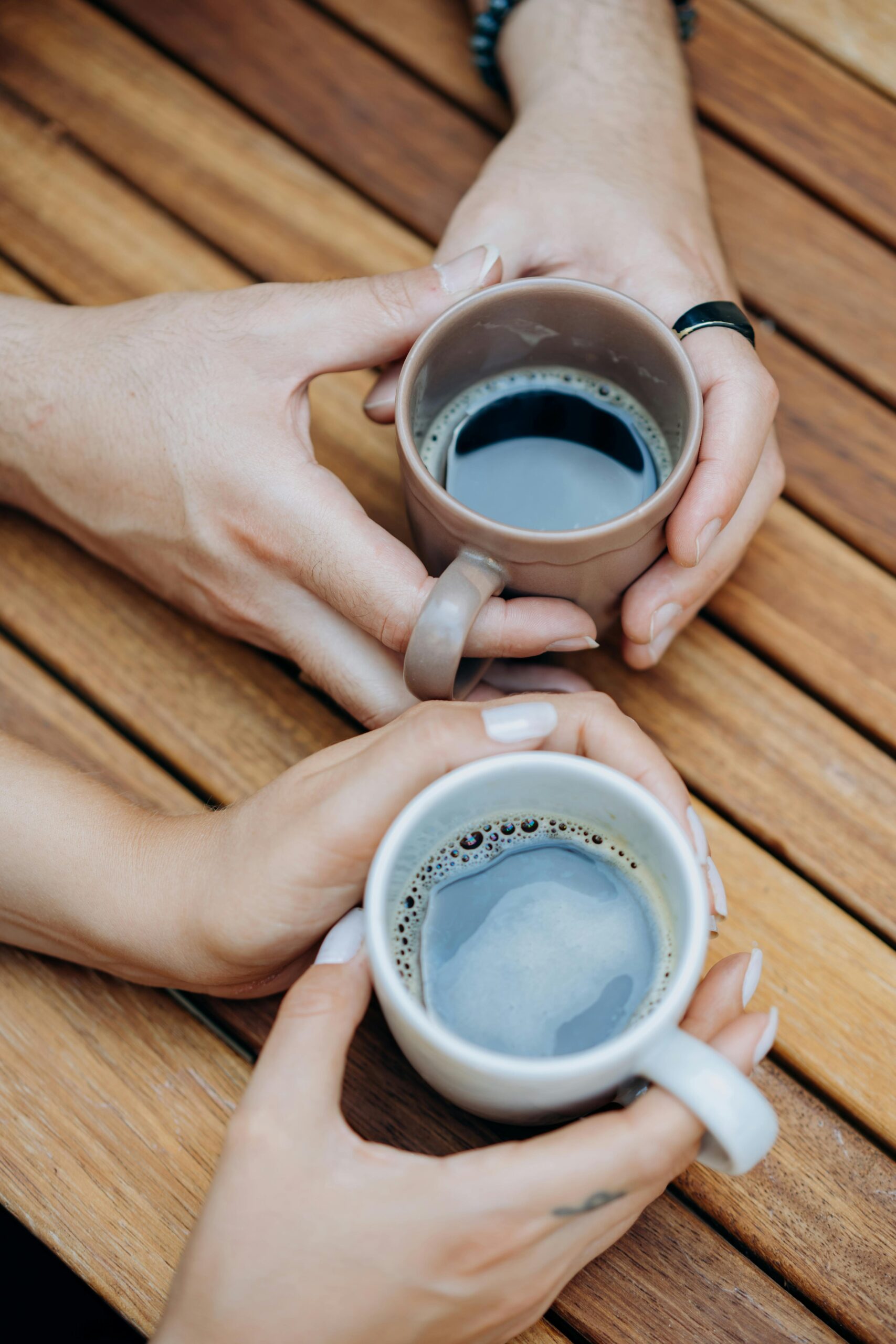 Two people holding coffee mugs over a wooden table, evoking warmth and connection.